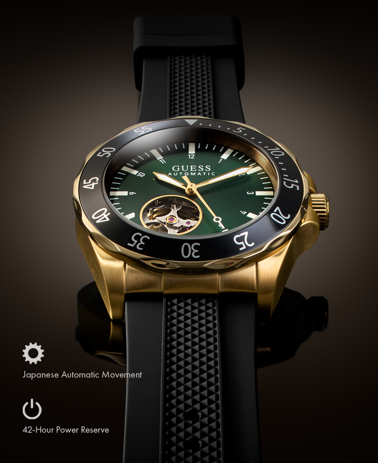 A Guess wristwatch with a gold-tone case, dark green dial, black bezel, and black textured strap, shown on a dark reflective studio background with feature icons and text in the lower left.
