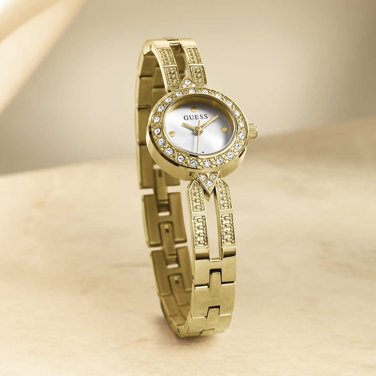 Gold watch with gemstone accents on a beige background