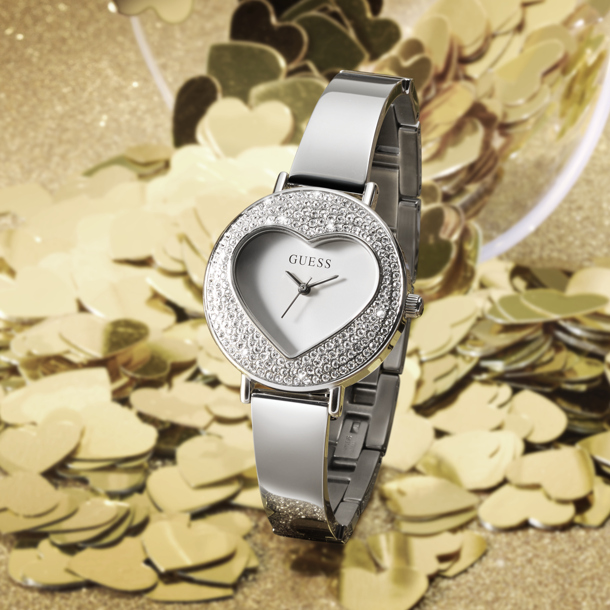 Silver GUESS heart shaped watch on glitter gold background
