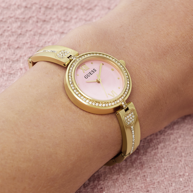 Gold watch with pink face on a wrist against a pink background