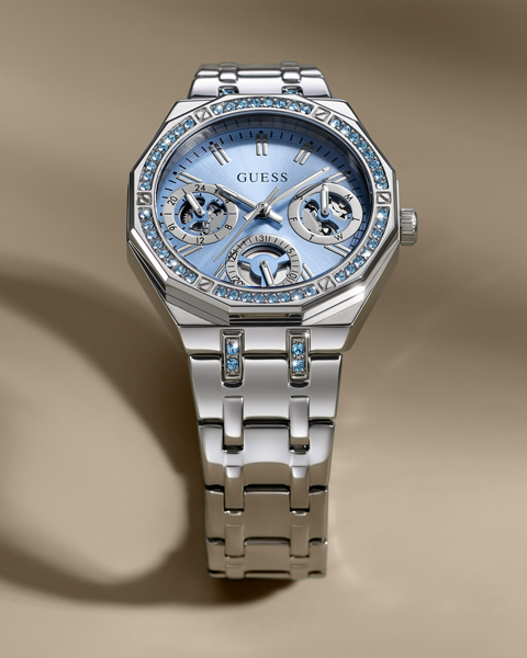 Silver Guess Swarovski watch with blue face on a beige background