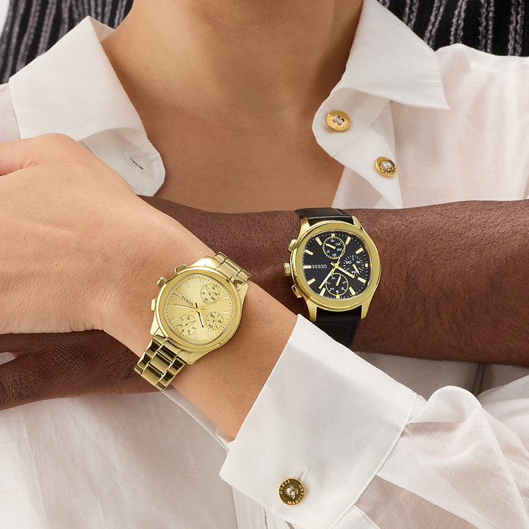 Two gold watches on a person's wrist with a white shirt background