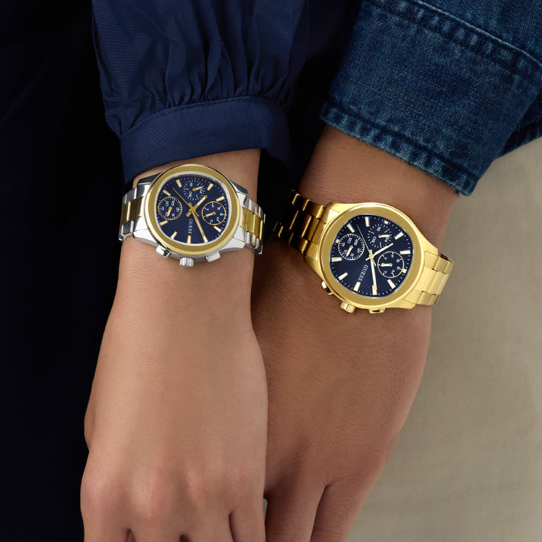 Two wristwatches, one silver and one gold, on a person's wrist against a neutral background.