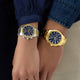 Two wristwatches, one silver and one gold, on a person's wrist against a neutral background.