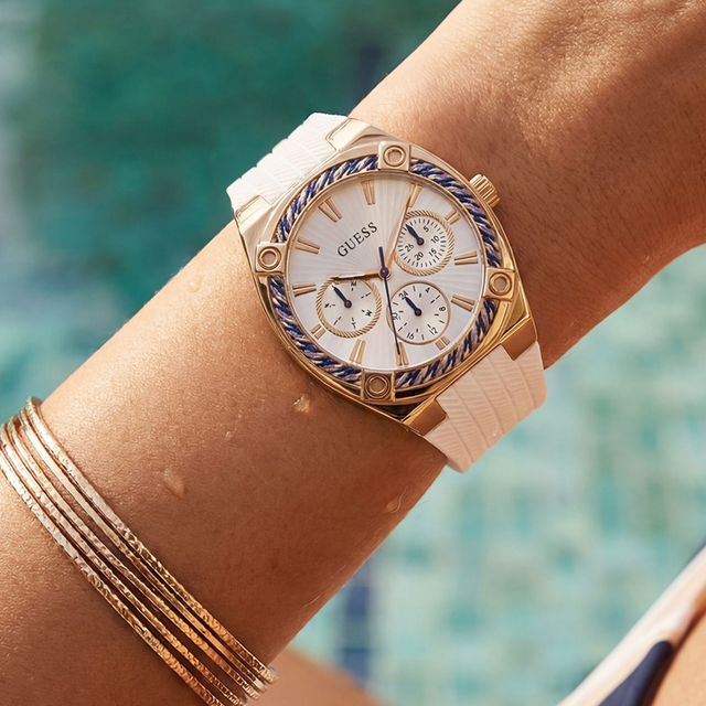 Gold watch with a white strap on a wrist against a blurred pool background
