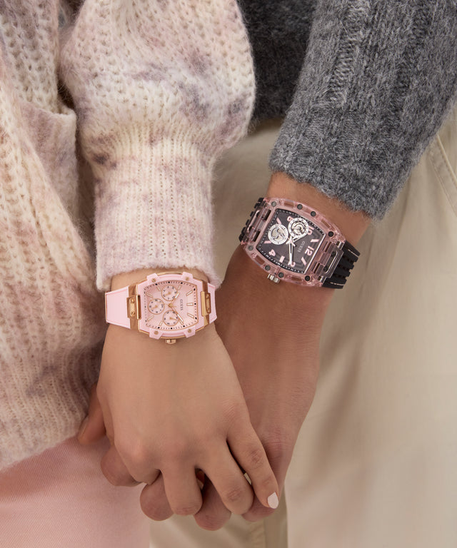 Two wrists wearing pink watches with detailed faces, held together.