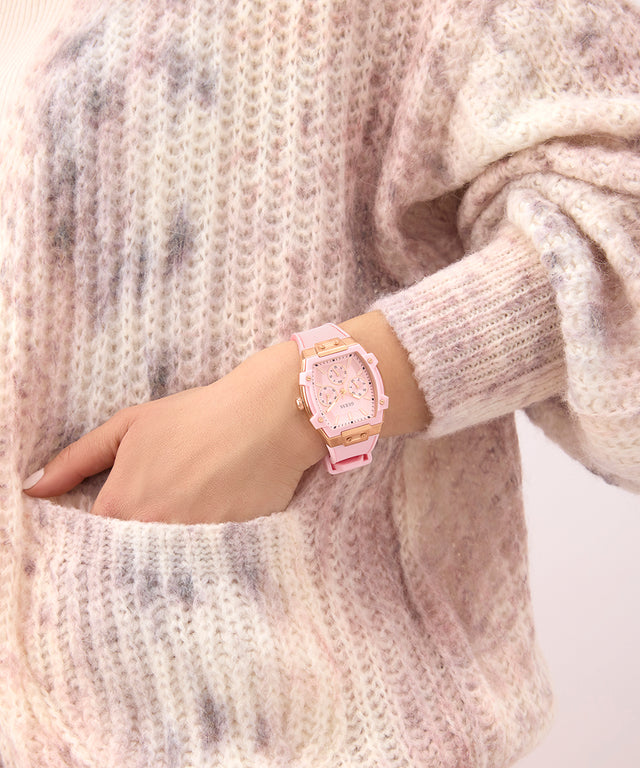 Hand wearing a GUESS Ladies Sparkling Pink Rose Gold Tone Multi-function Watch with a textured sweater background