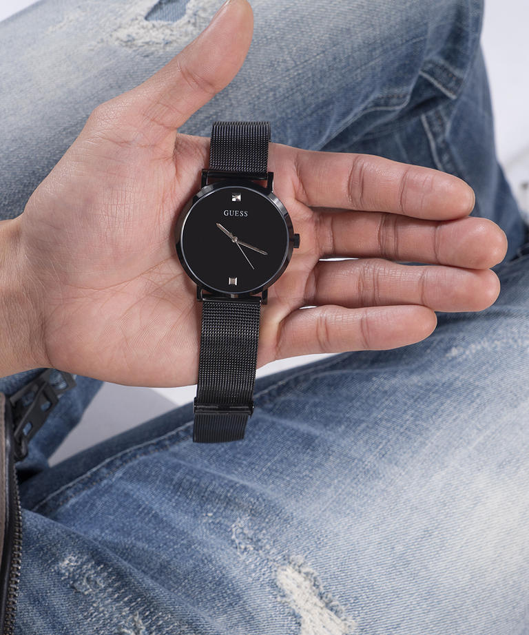 Person holding a black GUESS watch with a mesh band