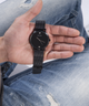 Person holding a black GUESS watch with a mesh band