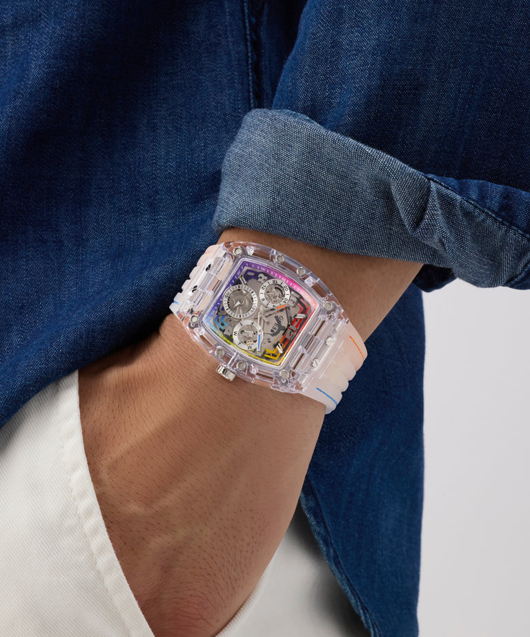 GUESS Mens Pride Limited Edition Clear Analog Watch  with a transparent case on a person's wrist, wearing a blue shirt.