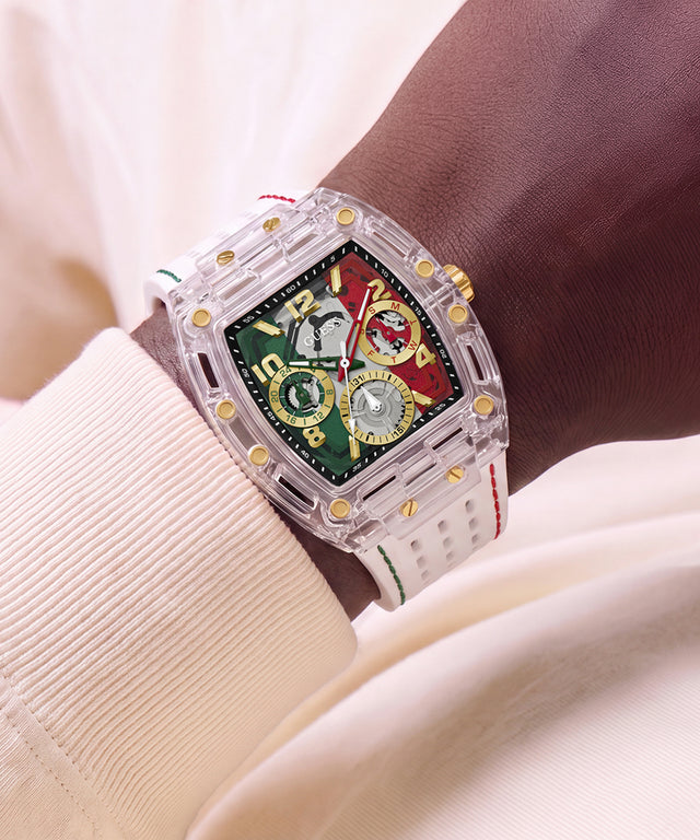 A sports watch with a transparent acrylic case, gold-tone accents, and a green and red dial, shown worn on a wrist with a cream-colored ribbed shirt in the background.