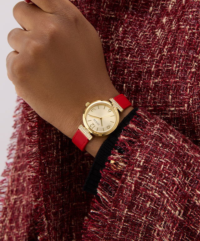 GUESS Ladies Red Gold Tone Analog Watch with a red strap on a hand wearing a red textured garment.