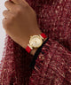 GUESS Ladies Red Gold Tone Analog Watch with a red strap on a hand wearing a red textured garment.