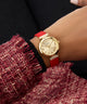 GUESS Ladies Red Gold Tone Analog Watch with a red strap worn on a wrist against a dark background