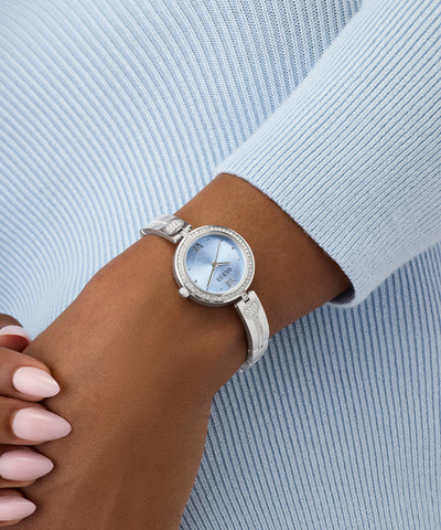 Silver GUESS Ladies Silver Tone Analog Watch on a wrist with a light blue background