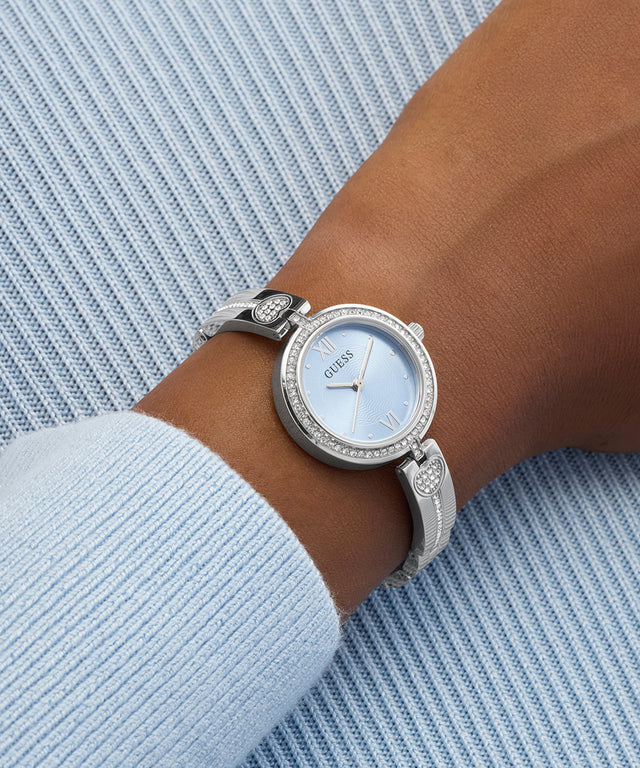 Silver GUESS Ladies Silver Tone Analog Watch with a light blue face on a wrist against a light blue textured background