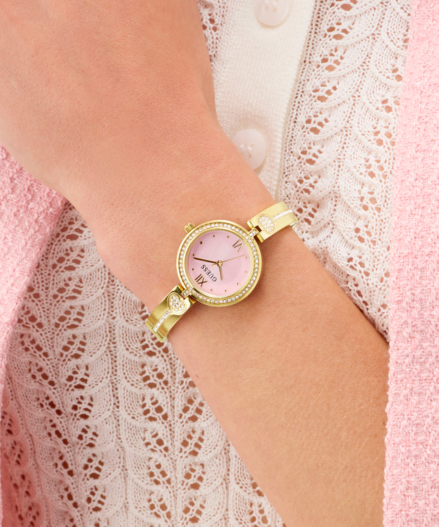 Gold GUESS Ladies Gold Tone Analog Watch with a pink face on a wrist against a lace garment background