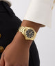 GUESS Ladies Gold Tone Multi-function Watch on a person's wrist with a neutral background