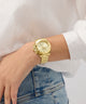Gold watch on a wrist with a white shirt and blue jeans