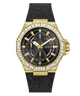 A gold-tone GUESS watch with an octagonal bezel set with clear stones, a black dial with three subdials, and a textured black strap, shown on a plain white background.
