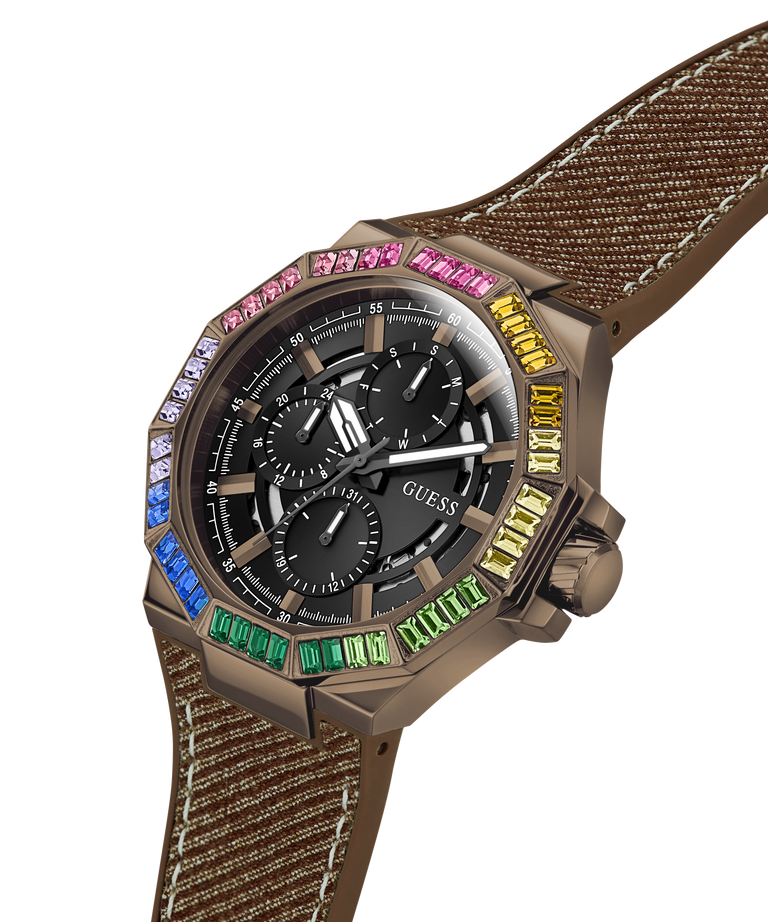 A GUESS chronograph watch with a brown textured fabric strap, a bronze-toned case, and a black dial. The octagonal bezel is decorated with colorful gemstones in blue, green, yellow, pink, and white. lifestyle