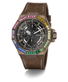 A GUESS wristwatch with a brown textured strap, a bronze-toned case, and a black dial surrounded by a vibrant rainbow bezel of colored gemstones, shown on a white background with a soft shadow.