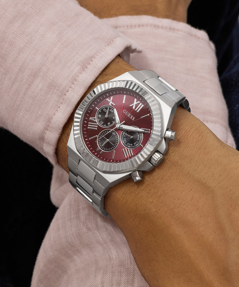 GUESS Mens Equity Silver Tone Analog Watch with a red face on a wrist, worn by a person in a light-colored shirt.