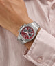 GUESS Mens Equity Silver Tone Analog Watch with a red face on a wrist, wearing a light pink shirt.