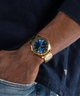 GW0718G2 GUESS Mens Gold Tone Analog Watch lifestyle watch on wrist and hand in pocket