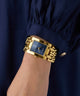 Gold GUESS Ladies Mod Heavy Metal Gold Tone Analog Watch on a wrist with a dark blue background