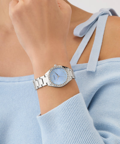 Silver GUESS Ladies Silver Tone Analog Watch on a wrist with a light blue top