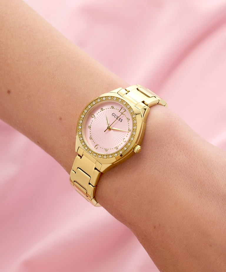 Gold GUESS Ladies Gold Tone Analog Watch with pink dial on a pink background