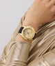 GUESS Ladies Black Gold Tone Multi-function Watch on a wrist with a plain background
