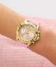 GUESS Ladies Pink Gold Tone Analog Watch with pink strap on a wrist against a pink background