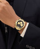 GUESS Mens Black Gold Tone Multi-function Watch on a person wearing a black suit with a white shirt.