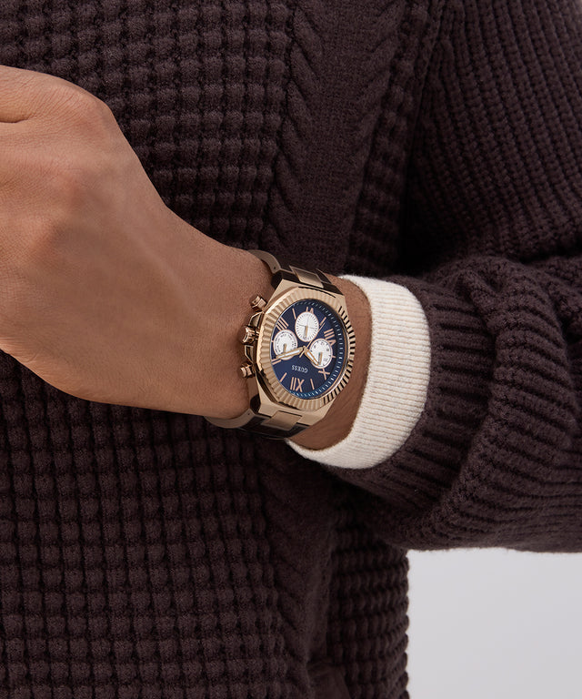 Close-up of a hand wearing a gold watch with a blue face on a brown textured sweater.