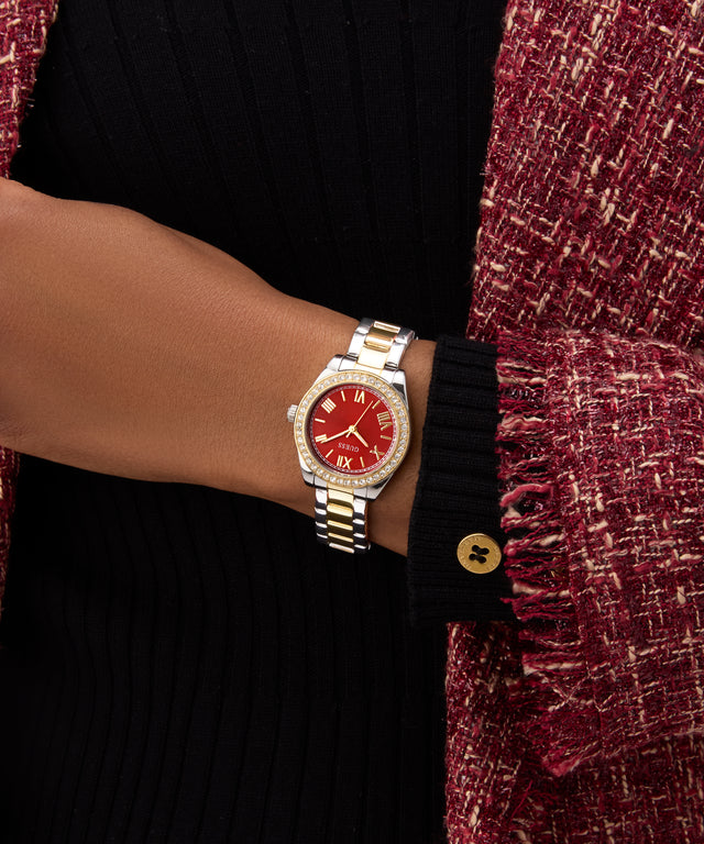 GUESS Ladies 2-Tone Analog Watch with a red face on a wrist, wearing a black sweater and maroon cardigan.