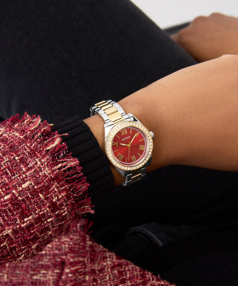 Gold and red GUESS Ladies 2-Tone Analog Watch on a wrist with a blurred background
