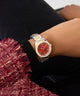 Gold and red GUESS Ladies 2-Tone Analog Watch on a wrist with a blurred background
