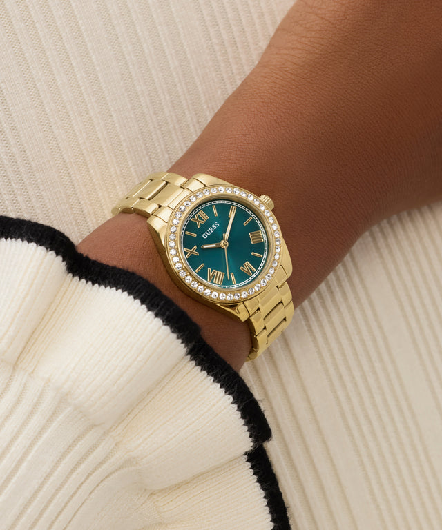 Gold watch with a teal face on a wrist against a neutral background