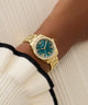 Gold watch with a teal face on a wrist against a neutral background