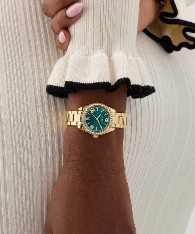 GUESS Ladies Mini Luna Gold Tone Analog Watch with a green face on a wrist against a neutral background