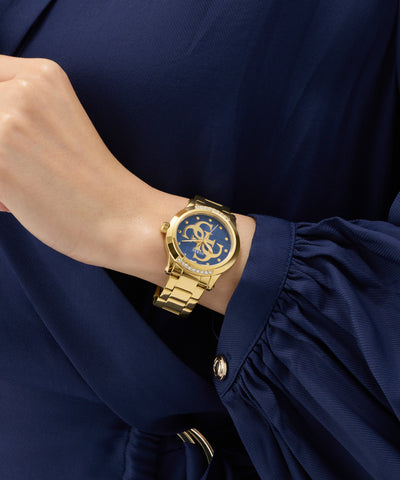 Gold GUESS Ladies Gold Tone Analog Watch on a wrist with a blue dress