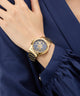 Gold GUESS Ladies Gold Tone Analog Watch on a wrist with a blue dress
