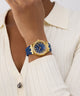 Gold watch with blue strap worn by a person in a white outfit GW0872L4