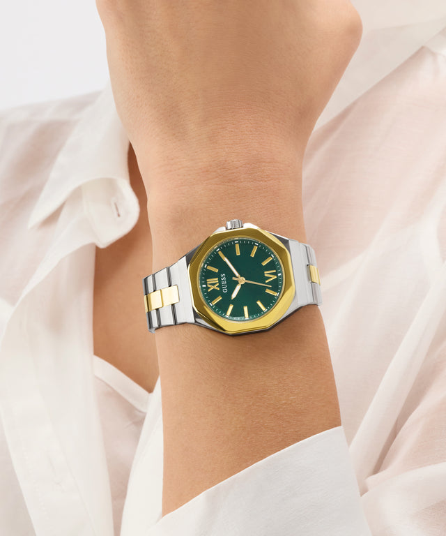 Gold and silver watch with green face on a wrist against a white background