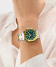 Gold and silver watch with green face on a wrist against a white background