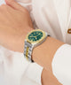 Wrist wearing a watch with a green face and gold accents on a white background