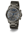 A GUESS men's chronograph watch with a dark gunmetal gray stainless steel case and integrated link bracelet, featuring a matching gray dial with blue accents, Roman numeral XII, and three subdials.