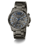 A GUESS men's chronograph watch with a dark gunmetal gray stainless steel case and integrated link bracelet, featuring a matching gray dial with blue accents, Roman numeral XII, and three subdials.
